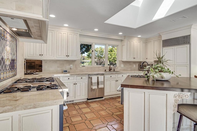 kitchen with sink, a breakfast bar area, tasteful backsplash, a skylight, and stainless steel dishwasher