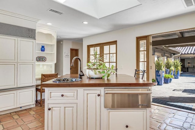 kitchen with a kitchen island with sink, light tile patterned floors, white cabinetry, and wooden counters