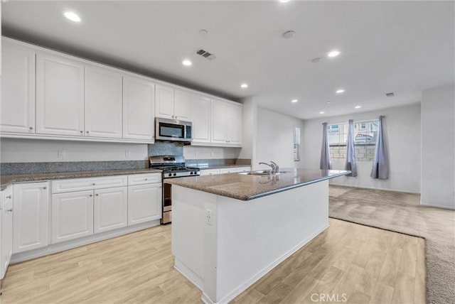 kitchen with light wood-type flooring, stainless steel appliances, an island with sink, and white cabinets