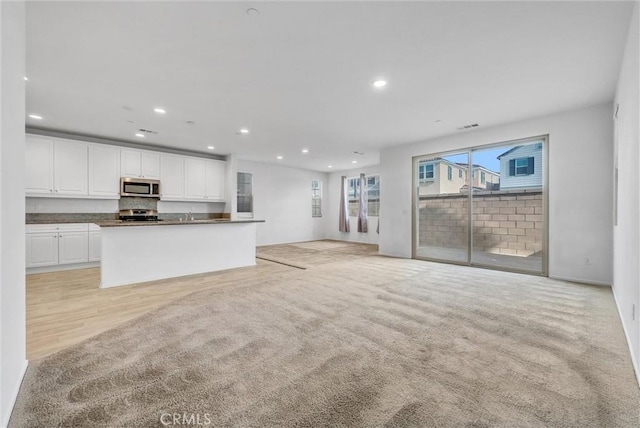 kitchen with light carpet, stainless steel appliances, a center island, and white cabinets