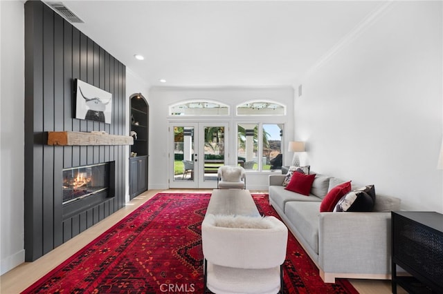 living room featuring french doors, a fireplace, built in shelves, and crown molding