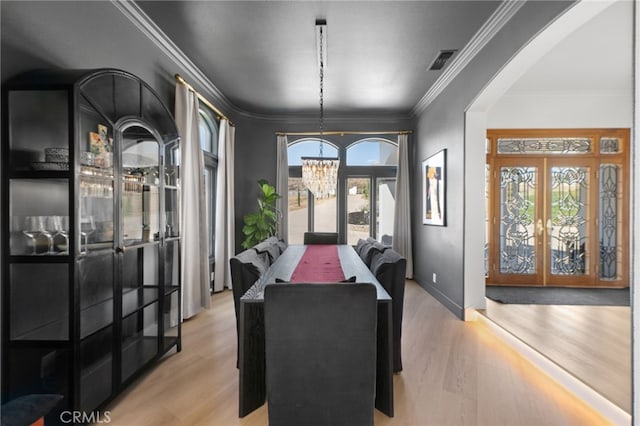 dining area with a notable chandelier, crown molding, french doors, and light wood-type flooring