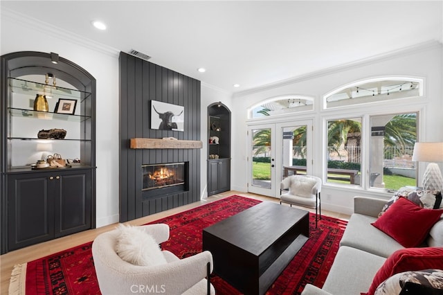 living room featuring built in shelves, ornamental molding, a fireplace, and light wood-type flooring