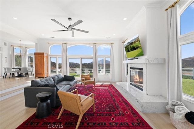 living room featuring ornamental molding, a premium fireplace, light hardwood / wood-style floors, and a wealth of natural light