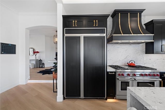 kitchen with crown molding, premium appliances, custom range hood, light hardwood / wood-style floors, and backsplash