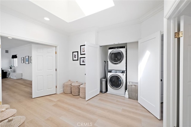 washroom featuring a skylight, light hardwood / wood-style flooring, ornamental molding, and stacked washing maching and dryer