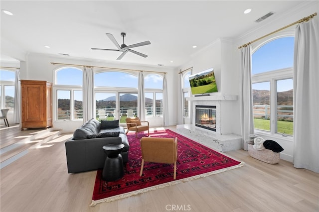 living room featuring crown molding, light wood-type flooring, ceiling fan, and a high end fireplace