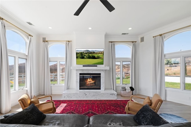 living room with ornamental molding, a high end fireplace, wood-type flooring, and a wealth of natural light