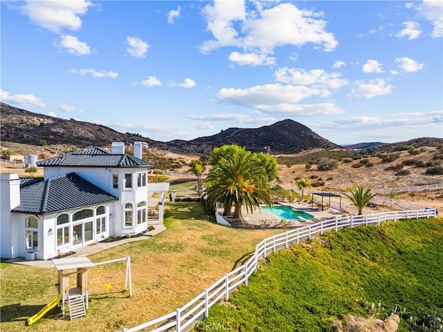 rear view of property featuring a fenced in pool, a mountain view, a yard, and a playground