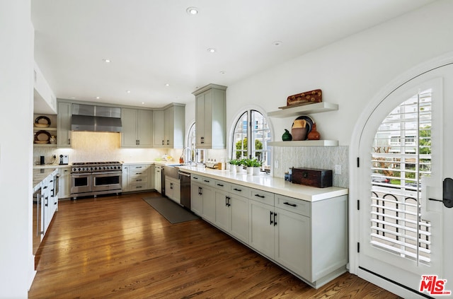 kitchen with gray cabinets, appliances with stainless steel finishes, tasteful backsplash, dark hardwood / wood-style flooring, and wall chimney exhaust hood