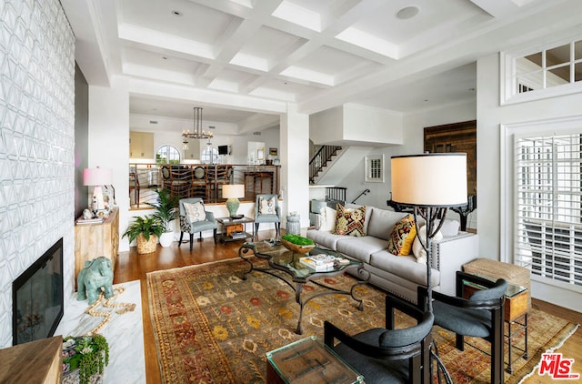 living room featuring beamed ceiling, a large fireplace, hardwood / wood-style flooring, coffered ceiling, and an inviting chandelier