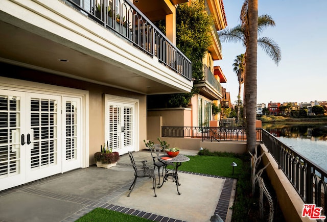 view of patio featuring a balcony, a water view, and french doors