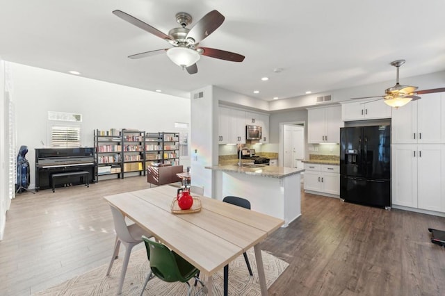 kitchen with range, light stone countertops, white cabinets, black fridge with ice dispenser, and kitchen peninsula