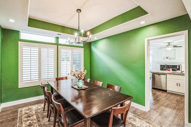 dining space featuring ceiling fan with notable chandelier, a tray ceiling, sink, and light hardwood / wood-style flooring