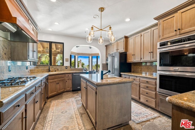 kitchen featuring custom exhaust hood, tasteful backsplash, decorative light fixtures, stainless steel appliances, and a kitchen island with sink