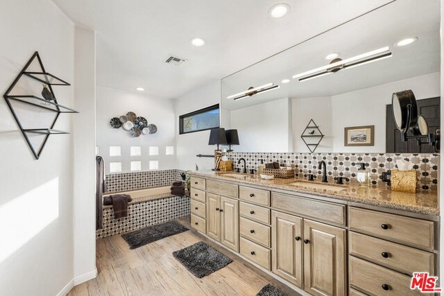 bathroom featuring hardwood / wood-style flooring, vanity, a tub, and decorative backsplash