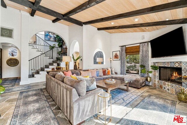 living room featuring wood ceiling, high vaulted ceiling, a tile fireplace, and beamed ceiling