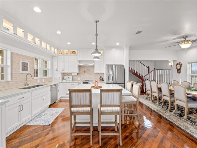 kitchen with a kitchen island, appliances with stainless steel finishes, white cabinetry, sink, and hanging light fixtures