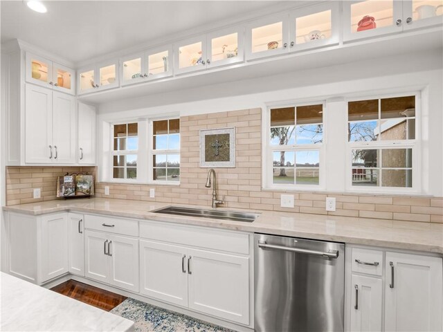 kitchen featuring white cabinetry, sink, backsplash, stainless steel dishwasher, and light stone counters