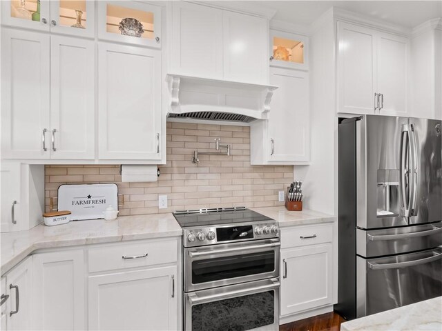 kitchen with light stone counters, appliances with stainless steel finishes, custom exhaust hood, and white cabinets