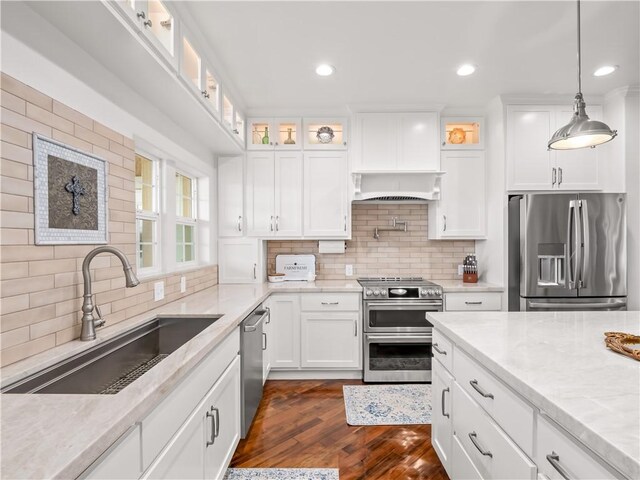 kitchen with sink, white cabinetry, hanging light fixtures, appliances with stainless steel finishes, and light stone countertops