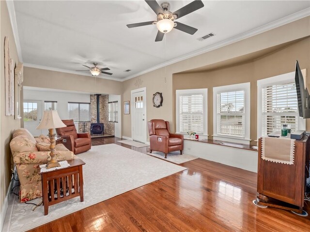 living room featuring crown molding, hardwood / wood-style flooring, ceiling fan, and a wood stove