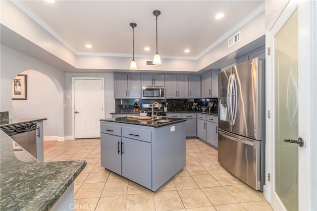 kitchen featuring sink, decorative light fixtures, appliances with stainless steel finishes, dark stone counters, and a kitchen island with sink