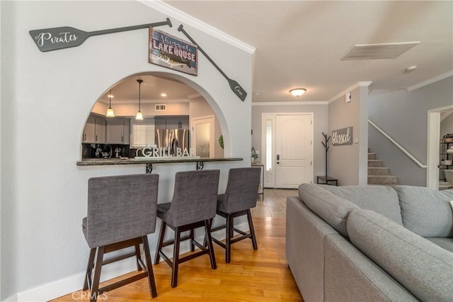 interior space featuring stainless steel refrigerator with ice dispenser, crown molding, light wood-type flooring, a kitchen breakfast bar, and kitchen peninsula