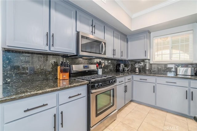 kitchen featuring decorative backsplash, ornamental molding, stainless steel appliances, and dark stone counters