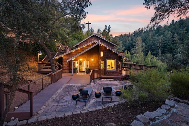 back house at dusk featuring a wooden deck, a patio area, and a fire pit