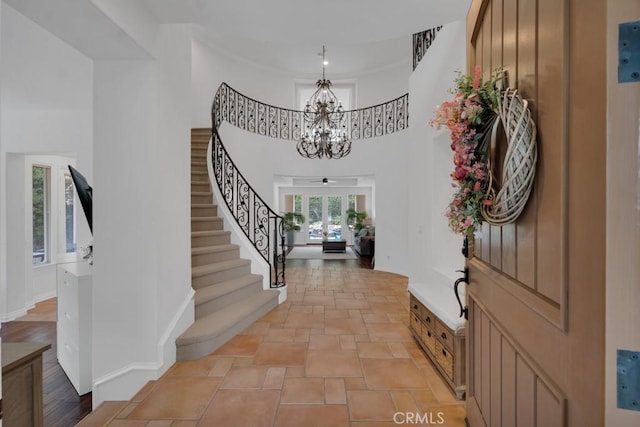 entrance foyer with baseboards, a towering ceiling, an inviting chandelier, and stairway