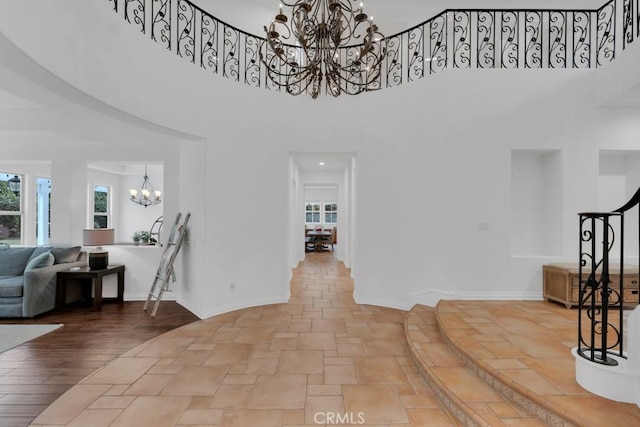 interior space featuring stairway, stone finish floor, baseboards, a high ceiling, and a notable chandelier