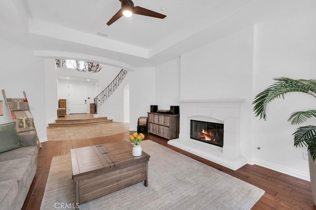 living room featuring hardwood / wood-style flooring, a raised ceiling, and ceiling fan