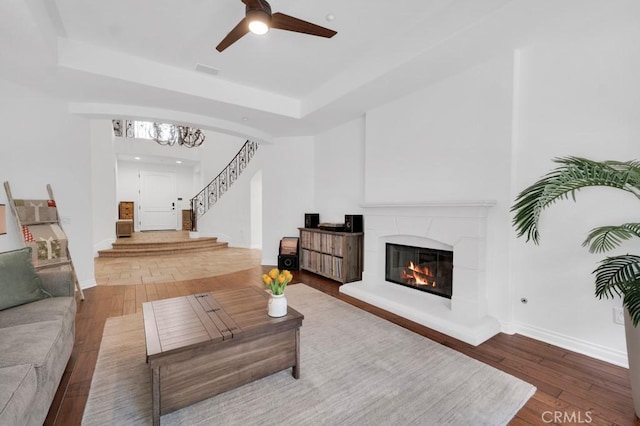 living area with a tray ceiling, stairs, hardwood / wood-style flooring, a glass covered fireplace, and visible vents