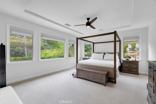 bedroom with a tray ceiling, light colored carpet, visible vents, and baseboards