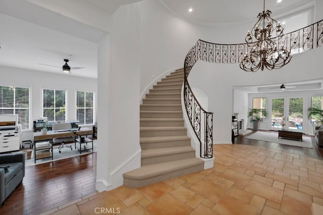 stairs with ceiling fan with notable chandelier, ornamental molding, a healthy amount of sunlight, and a high ceiling