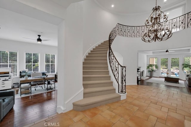 stairway with baseboards, a towering ceiling, ceiling fan with notable chandelier, and a wealth of natural light