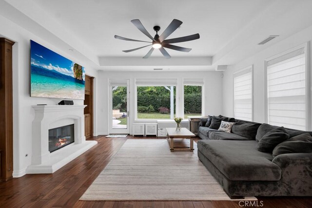 living room featuring radiator, a tray ceiling, dark wood-type flooring, and ceiling fan