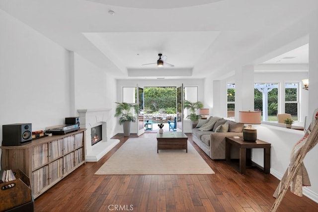 living room featuring dark wood-type flooring, a raised ceiling, and ceiling fan