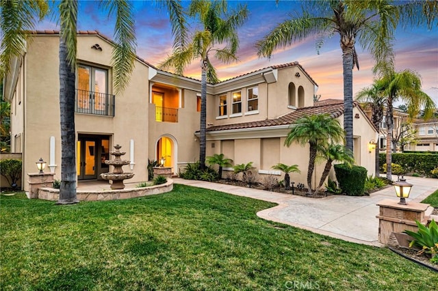 mediterranean / spanish-style home with a tile roof, stucco siding, french doors, a balcony, and a front yard