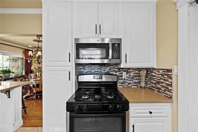 kitchen with stainless steel microwave, decorative backsplash, ornamental molding, white cabinets, and gas range