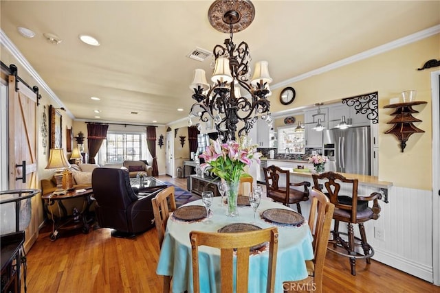 dining room featuring a chandelier, a barn door, wood finished floors, visible vents, and crown molding