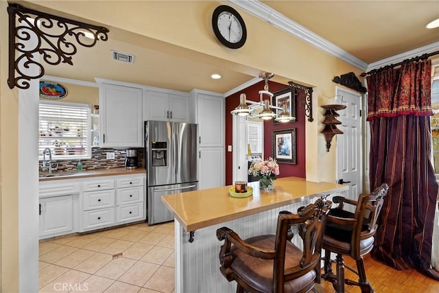 kitchen with a sink, visible vents, tasteful backsplash, stainless steel fridge, and crown molding