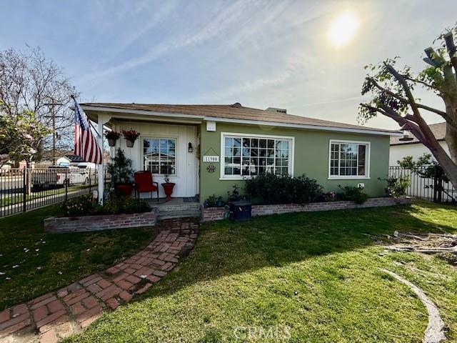 view of front of house featuring fence, a front lawn, and stucco siding