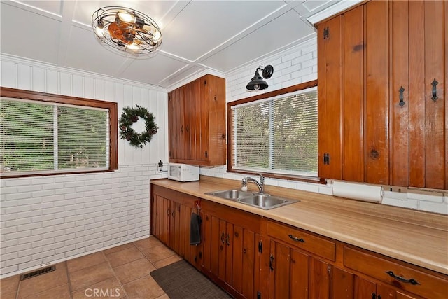 kitchen featuring brick wall, sink, light tile patterned floors, and plenty of natural light