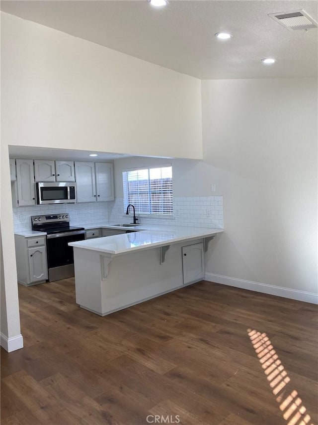 kitchen featuring sink, gray cabinetry, stainless steel appliances, a kitchen bar, and kitchen peninsula