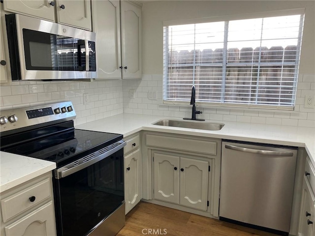 kitchen featuring appliances with stainless steel finishes, sink, white cabinets, backsplash, and light hardwood / wood-style flooring