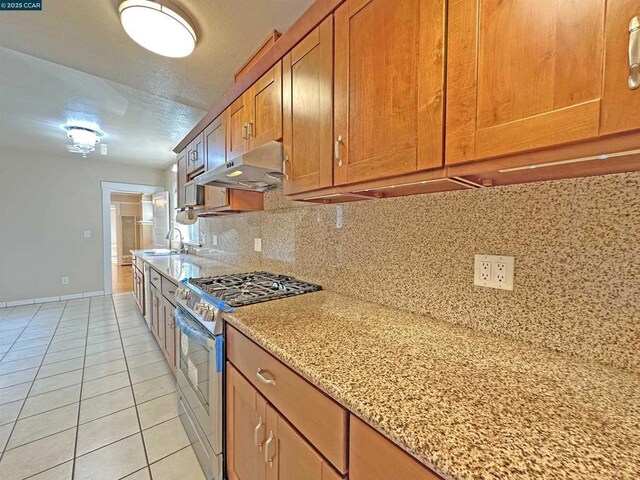 kitchen with light tile patterned flooring, sink, stainless steel gas range oven, light stone counters, and backsplash