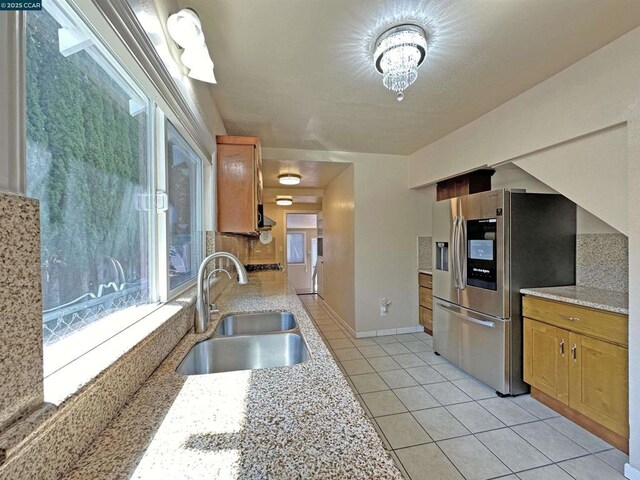 kitchen with light stone counters, stainless steel fridge with ice dispenser, sink, and light tile patterned floors