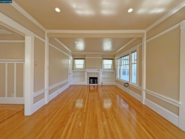 unfurnished living room with crown molding, plenty of natural light, a stone fireplace, and hardwood / wood-style flooring